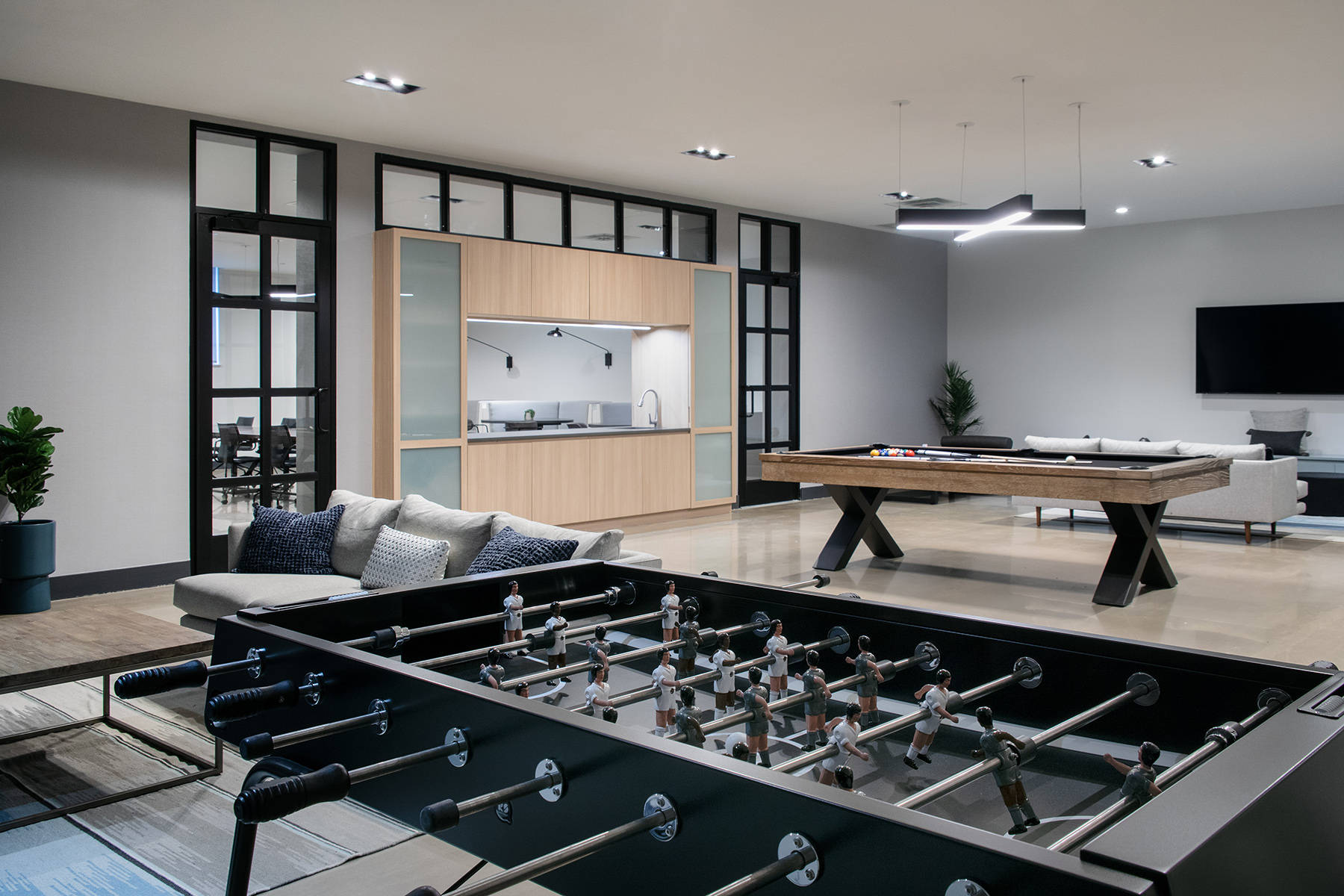 Game room with close up of foosball table with billiards talbe, couches and kitchen in the background