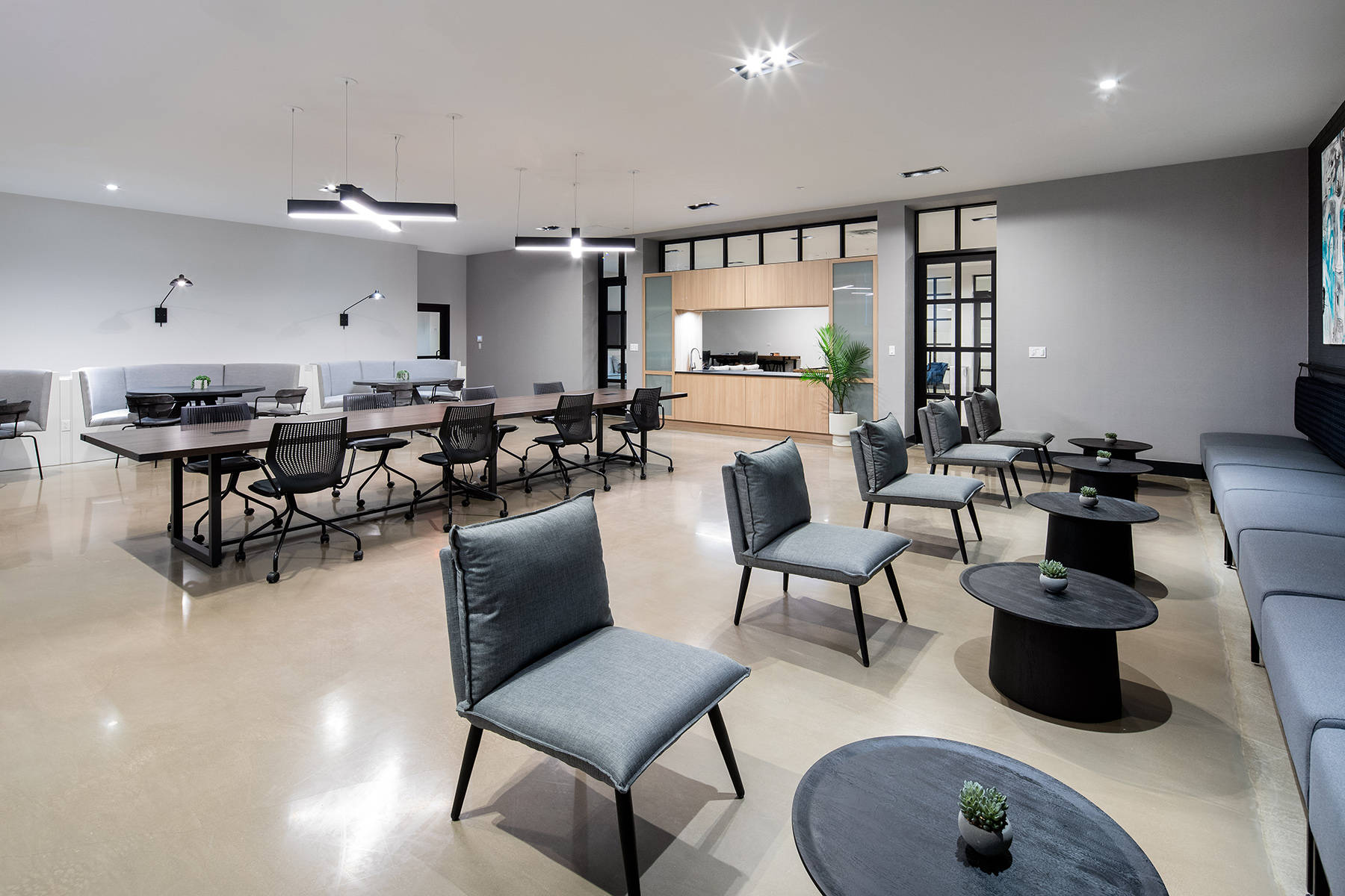 Coworking room with ample seating including large conference table and smaller side tables with modern seating plus kitchen